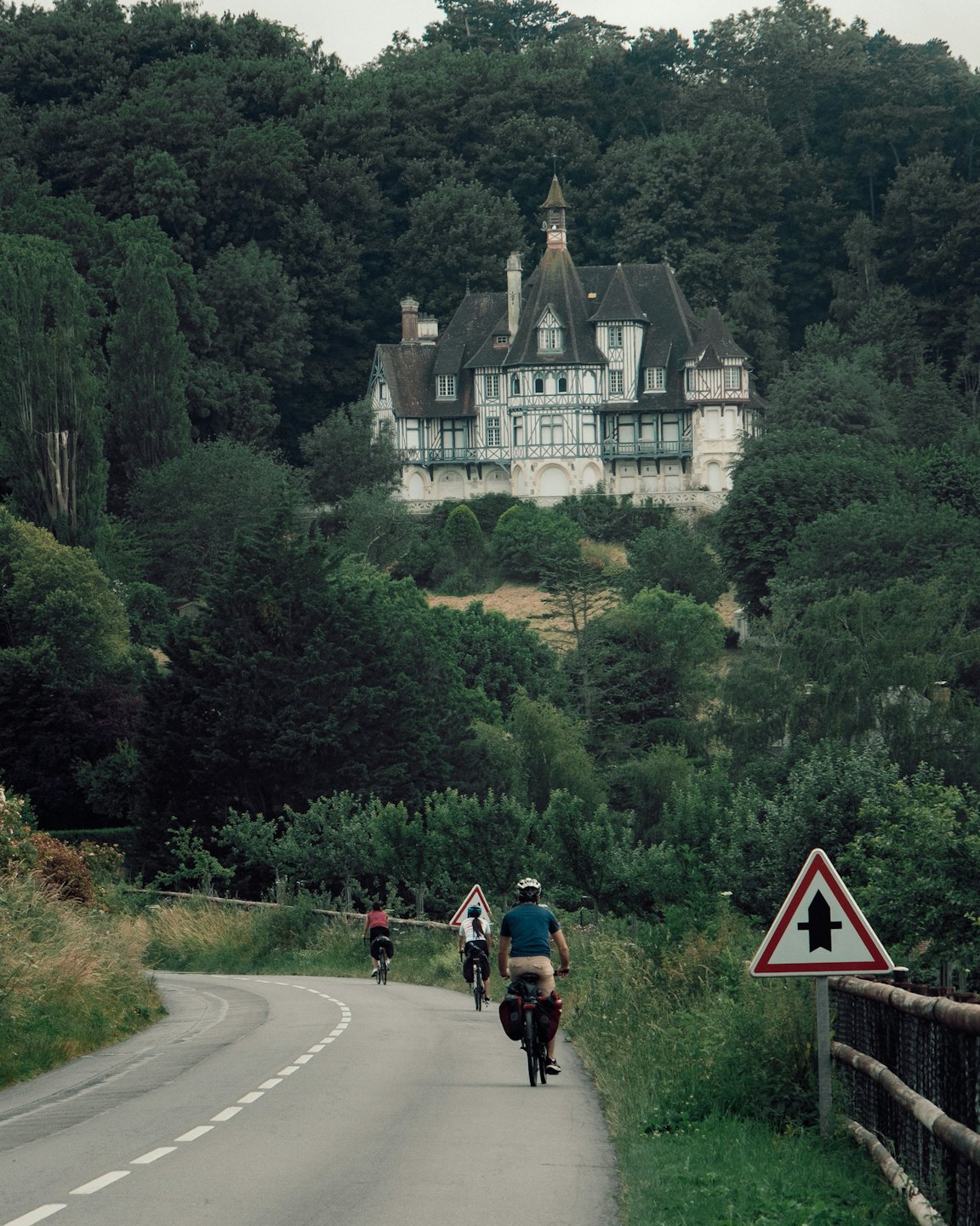 Tre ciclisti pedalano su una strada verso una casa storica.
