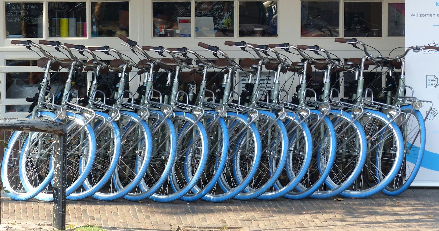File di biciclette a noleggio con ruote blu parcheggiate su mattoni all'esterno.