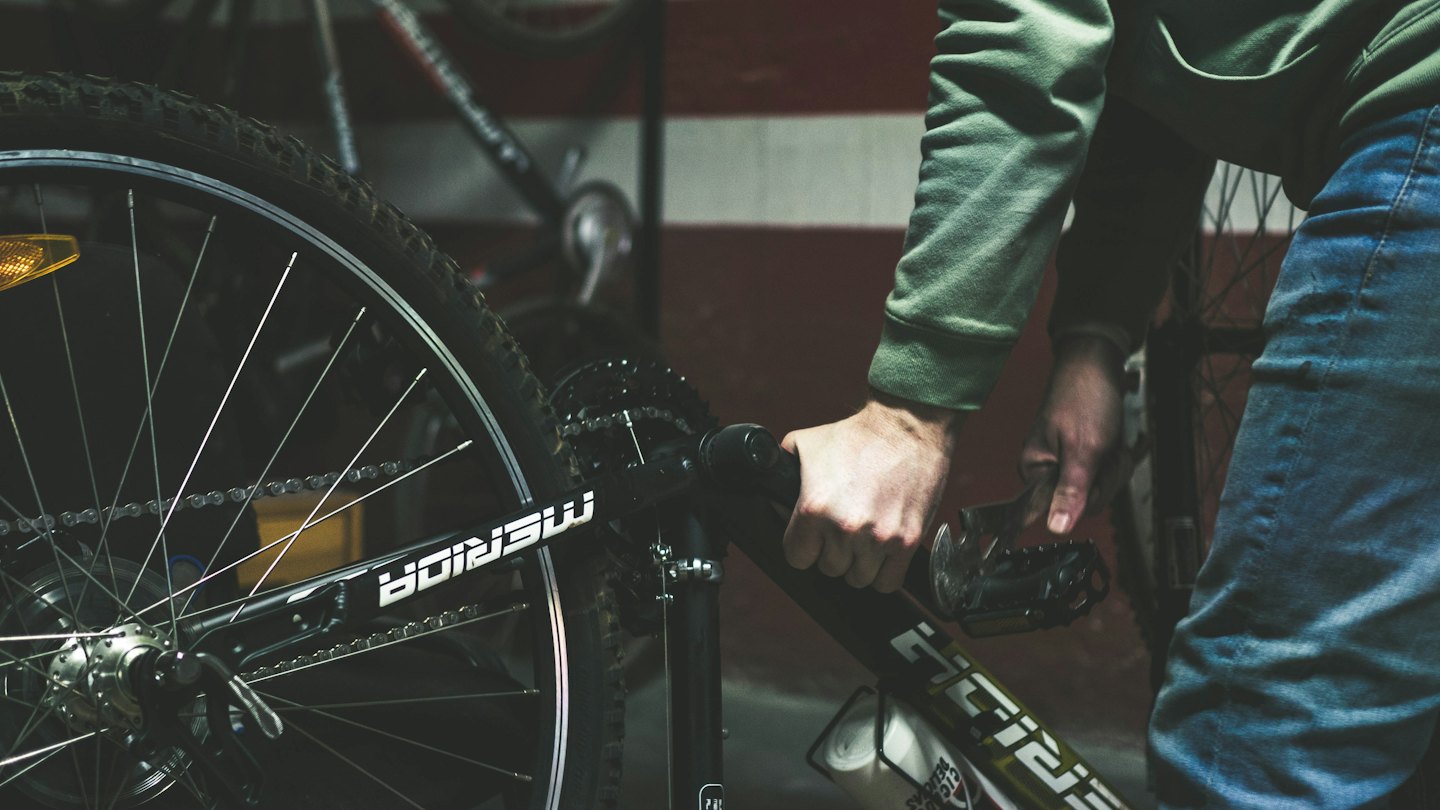 Mani che puliscono la catena di una mountain bike nera.